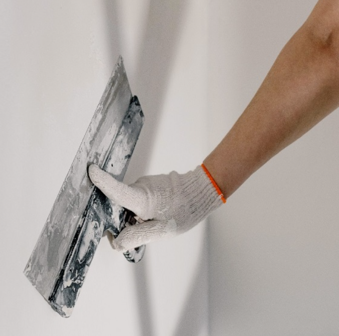 Main tenant une spatule appliquant de l'enduit sur un mur